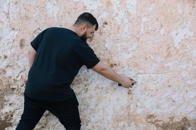 Rear view of a man painting graffiti on damaged wall