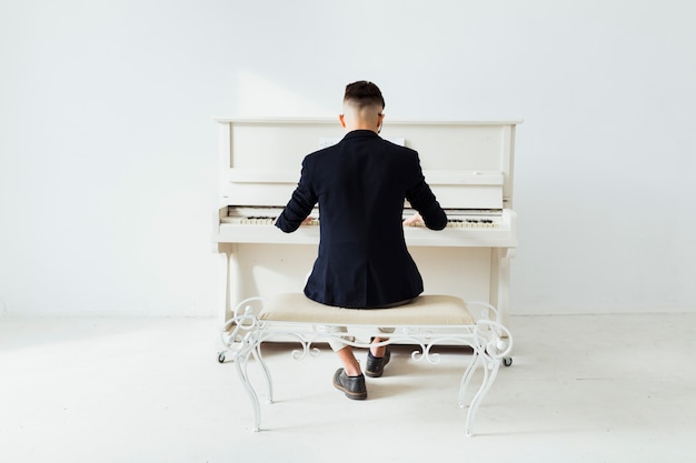 白い壁に座ってピアノを弾く男の背面図