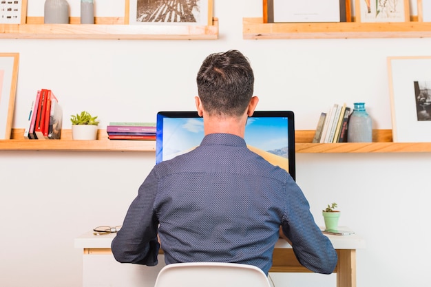 Rear view of man sitting on chair using computer in office