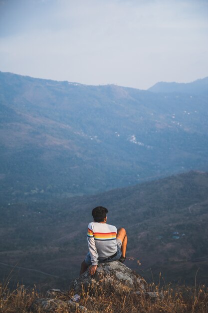 自然を考えている岩の上に座っている男の背面図。
