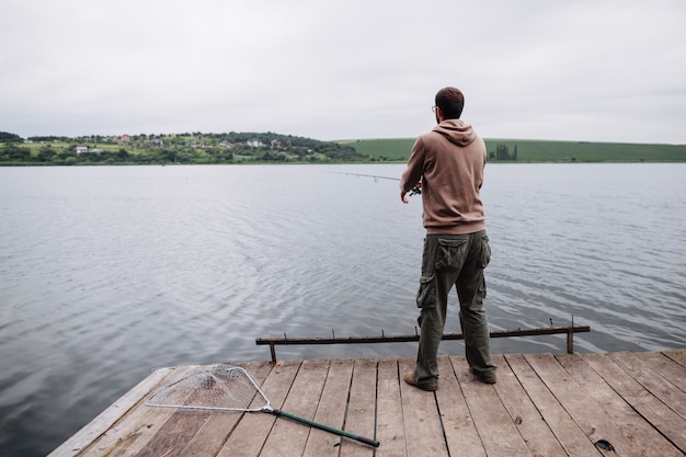 Вид сзади человека, стоящего на пирсе, рыбалка в озере
