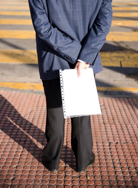 Rear view of a man standing on sidewalk holding white folder in hand