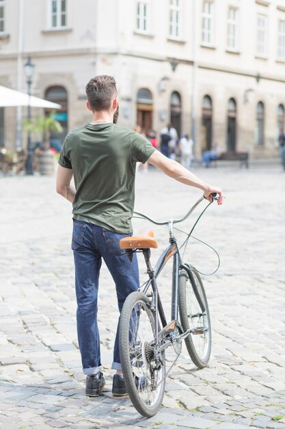 Rear view of a man standing with his bicycle in city