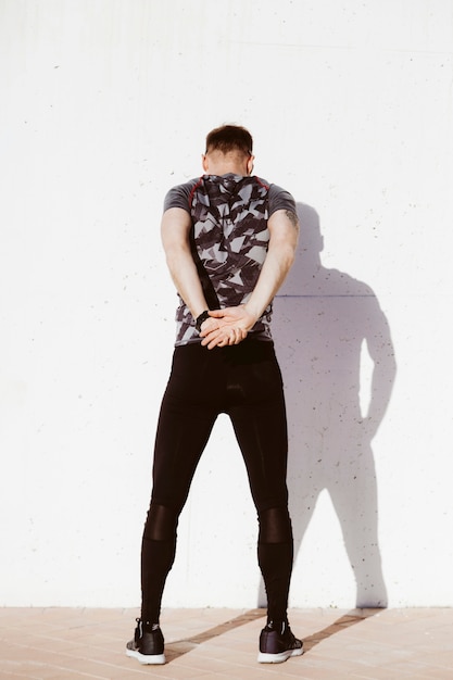 Free photo rear view of man stretching arms behind back in front of white wall