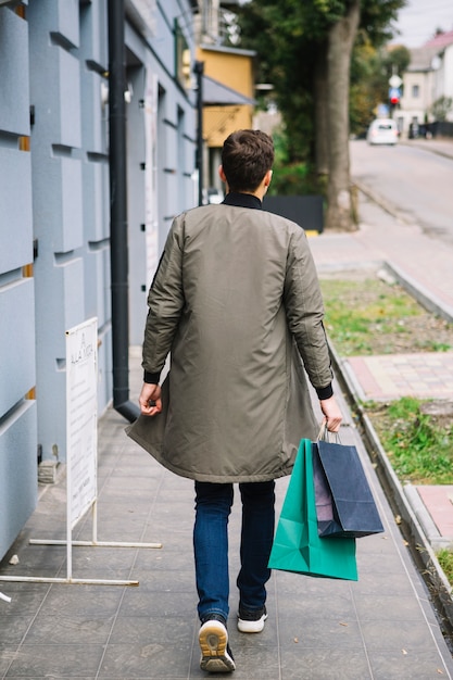Rear view of a man walking on sidewalk holding shopping bags