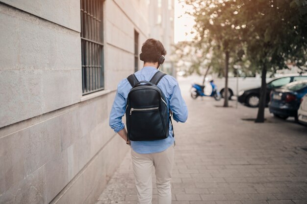 Rear view of a man with black backpack walking on pavement