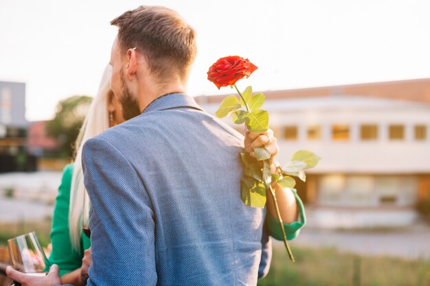 Вид сзади человека со своей девушкой, держащей красивую красную розу в руке