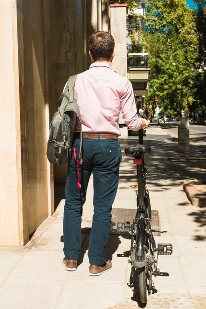 Вид сзади человека с его рюкзаком, идущим с велосипедом