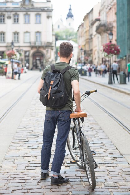 Rear view of a man with his bicycle standing on street