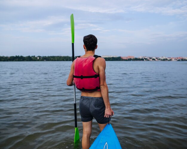 Вид сзади человека с веслом и байдаркой у берега озера