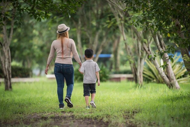 Rear view of mother and son walking together in home garden holding hand. 