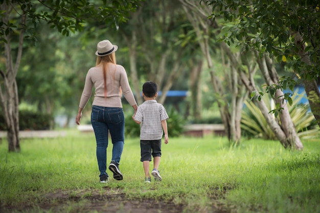 어머니와 아들이 손을 잡고 집 정원에서 함께 걷는 후면보기.