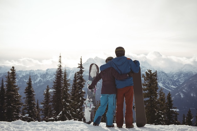 Бесплатное фото Вид сзади пара, держащая сноуборд на горе зимой против неба