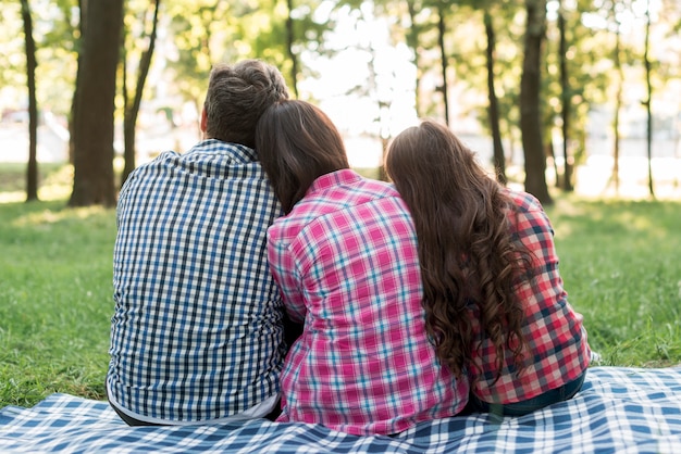 Бесплатное фото Вид сзади семьи, сидя в парке с головой на плече друг друга