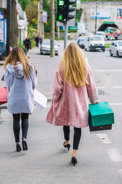 通りを歩いて手に買い物袋を保持している2人の金髪の若い女性の後姿