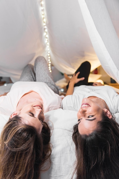 Бесплатное фото Вид сзади молодых женщин, лежащих на кровати под белым занавесом