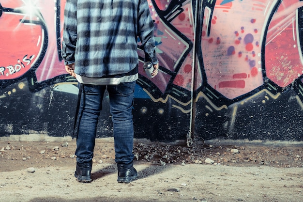 Вид сзади человека, стоящего перед граффити, держащего бутылку с распылителем