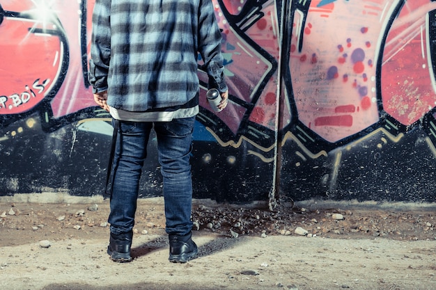 Foto gratuita retrovisione della persona che sta davanti alla bottiglia dello spruzzo della tenuta della parete dei graffiti