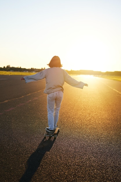 Rear view photo of young girl riding skateboard towards sunlight happy young woman on her cruiser sk