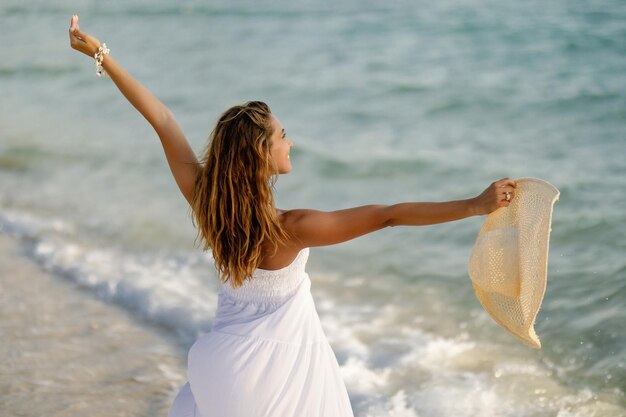 Rear view of playful woman enjoying in summer day while standing at the shore with her arms outstretched