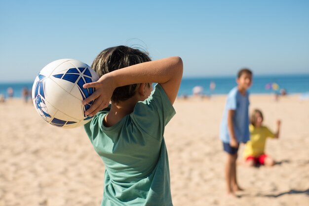 Rear view of preteen boy throwing ball on beach