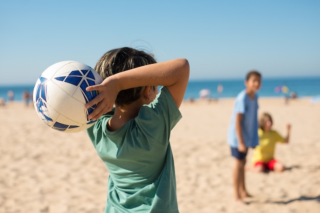 Вид сзади подросткового мальчика, бросающего мяч на пляже