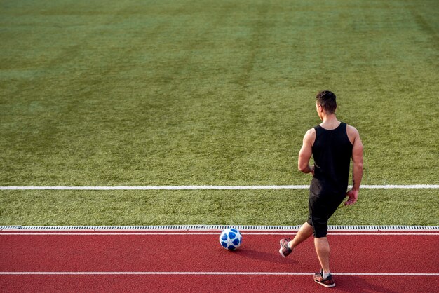 Rear view of a sportsperson playing on race track with soccer ball