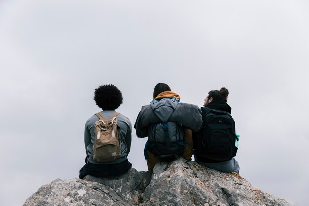 Rear view of a three friends sitting on rock against sky