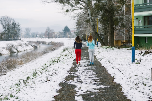 Rear view of two female friends jogging on road in winter