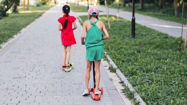 公園のプッシュスクーターに乗っている2人の女の子の背面図