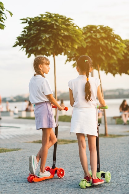 Rear view of two girls standing on push scooter in the park