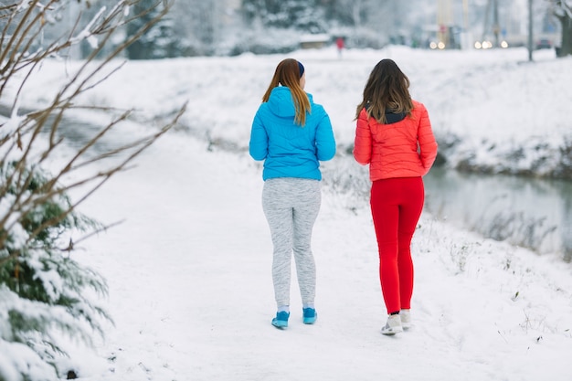 Rear view of two women walking together on frozen landscape in winter