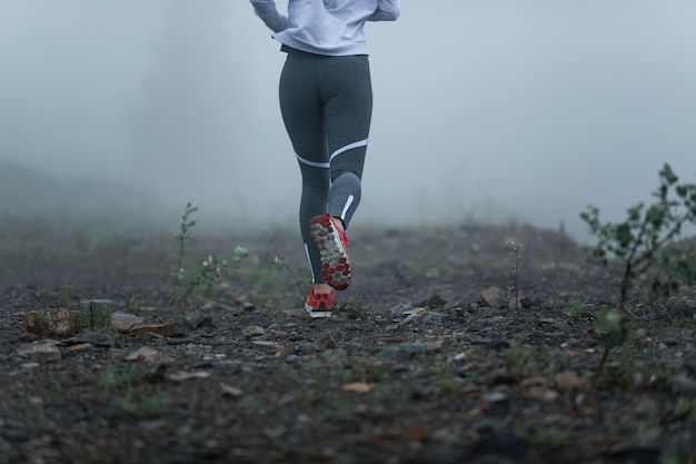 Retrovisione della donna atletica irriconoscibile che corre nella nebbia