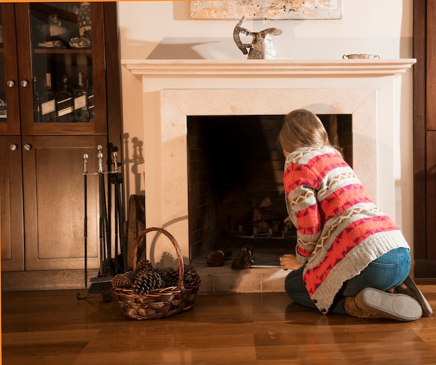 Rear view of woman arranging firewood in the fireplace at home