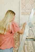 Free photo rear view of woman carving on wall with tool