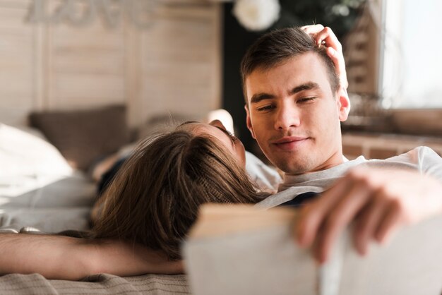 Rear view of woman lying on bed near the man reading book