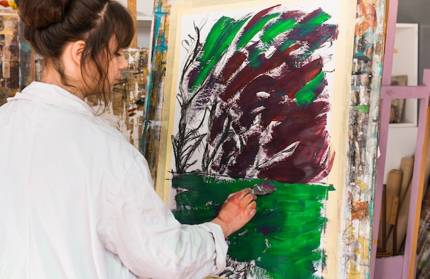 Rear view of woman painting on messy canvas at workshop