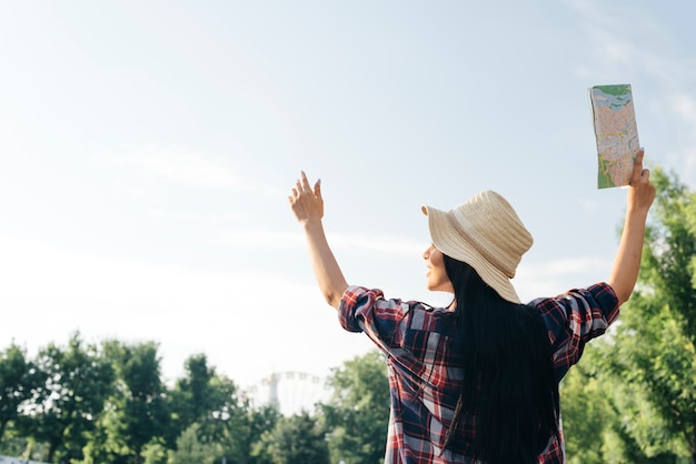 Rear view of woman raised her arm with holding map looking away