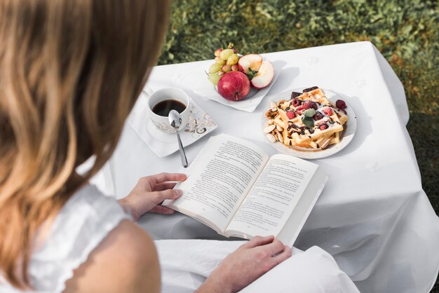 Rear view of a woman reading book with morning healthy breakfast on table at outdoors