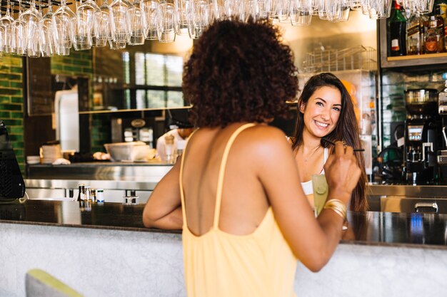 Rear view of woman sitting at bar counter in front of smiling woman