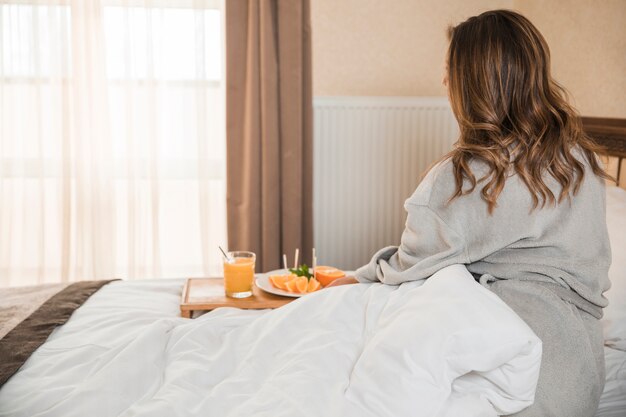 Rear view of woman sitting on bed having the healthy breakfast