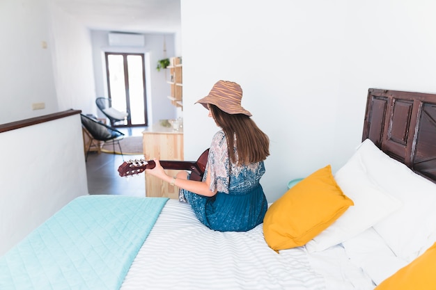 Rear view of a woman sitting on bed playing guitar