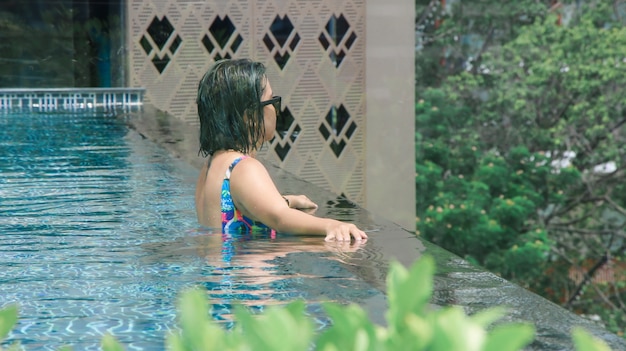 Вид сзади женщины, плавающей в расслабляющий бассейн с широкими распростертыми объятиями на кристально чистой воде.