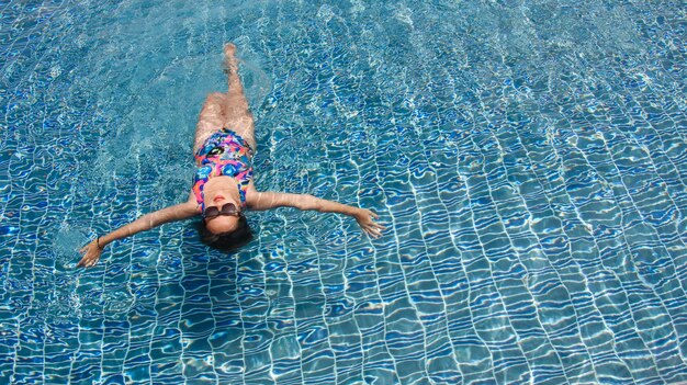 Rear view of a woman swimming at relaxing pool with wide open arms on crystal clear water.