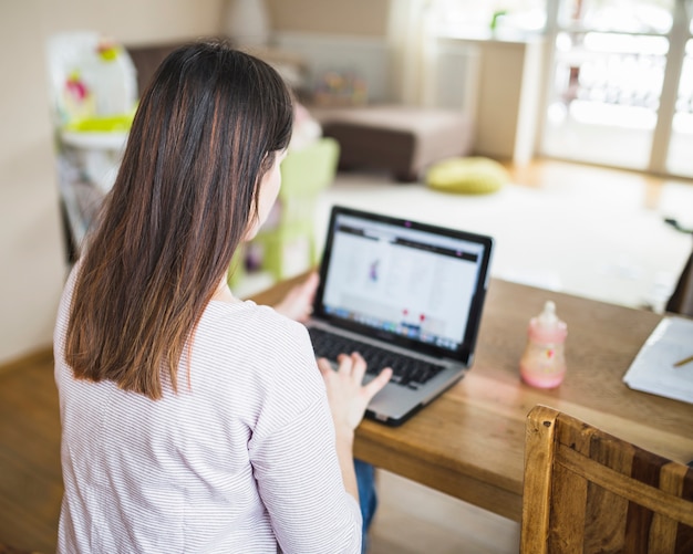 Rear view of a woman using laptop on wooden table