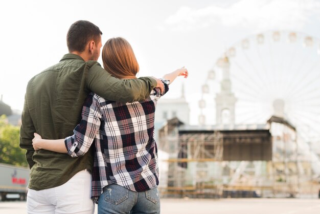 Rear view of woman with her boyfriend pointing at ferris wheel while