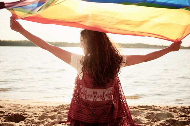 Vista posteriore di una donna con bandiera arcobaleno sulla spiaggia