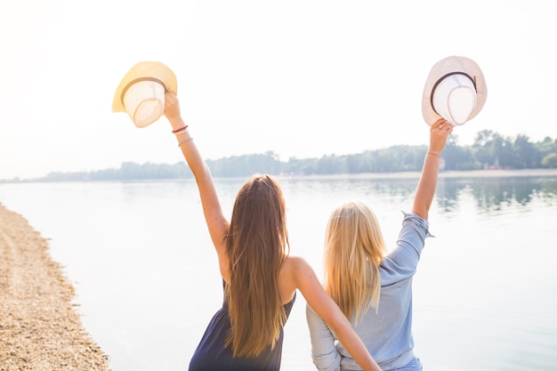 Rear view of women standing near the lake holding hat