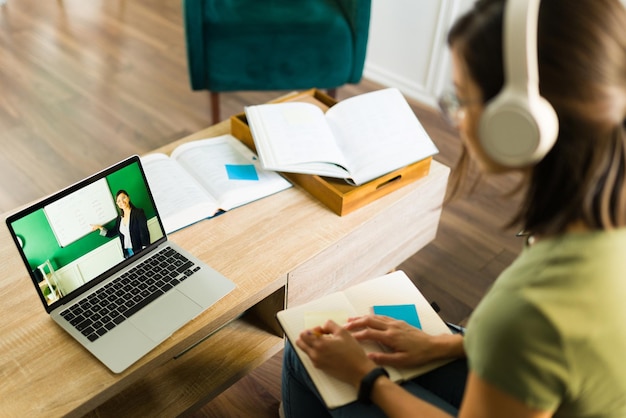 Rear view of a young college student paying attention and listening to her online teacher on the laptop at home