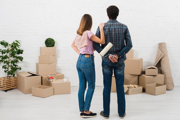 Rear view of young couple looking at the white painted wall with cardboard boxes